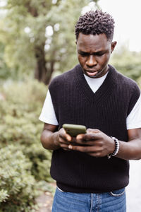 Young sad african man typing message, texting on phone outdoor