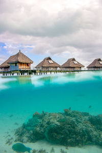 Stilt houses in sea against cloudy sky