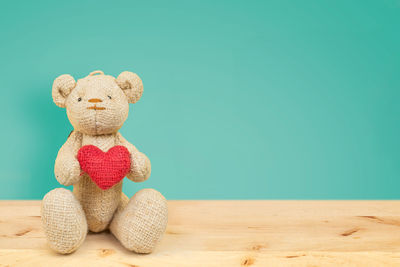 Close-up of teddy bear with heart shape on wooden table against blue background
