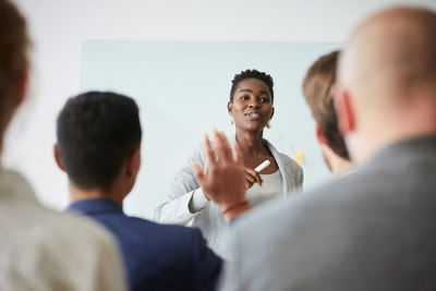 Smiling businesswoman talking with colleagues during presentation while standing in office seminar