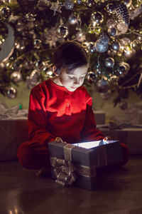 Merry christmas kid. boy child in red pyjamas sits on the floor and stares into the gift box.