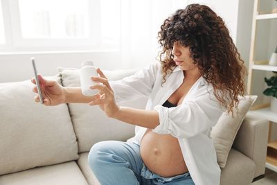 Young woman using phone while sitting on sofa at home