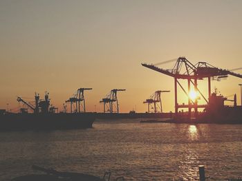 Cranes at commercial dock against sky during sunset