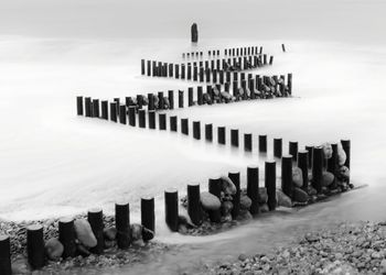 Wooden posts on beach during winter against sky