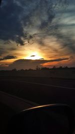 Scenic view of landscape against cloudy sky at sunset