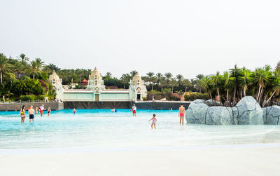 People swimming in pool against clear sky