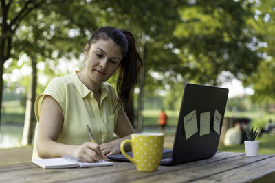 Woman with laptop writing on table in park