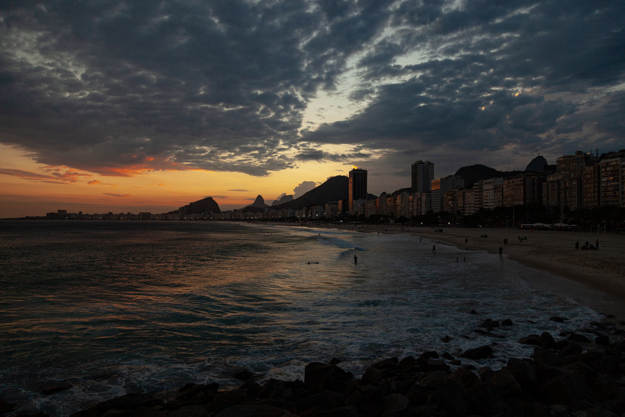 SCENIC VIEW OF SEA BY BUILDINGS AGAINST SKY DURING SUNSET