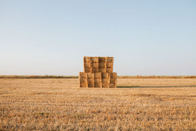 Stack of hay bales on field against clear sky