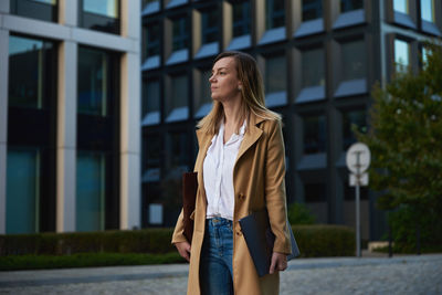 Business woman walking at city street with laptop at summer day. remote work