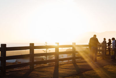 People standing by railing against sky during sunset