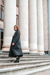 Young brunette woman walking up on stairs. long beautiful hair and long coat in business downtown. 