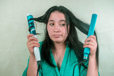 Close-up of young woman holding curling tongs and hair straightener