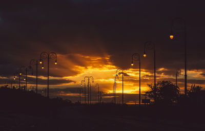 Silhouette street lights against orange sky at sunset