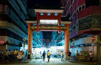 People walking on illuminated street amidst buildings in city at night