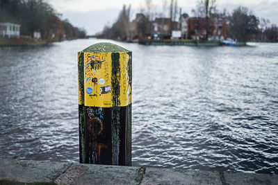 Close-up of yellow sign on wooden post in lake