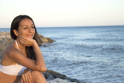 Smiling woman sitting on rock against sea 
