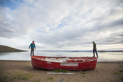 Two men stand on the edge of a retired red whaling boat.