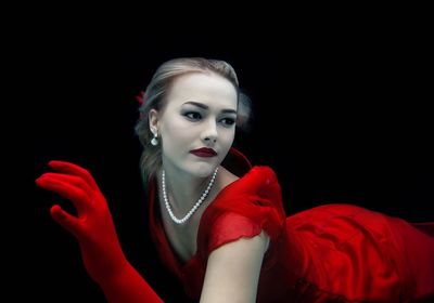 Beautiful young woman in red dress lying over black background