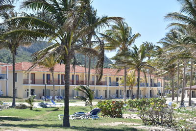 Built structure by palm trees and plants against sky