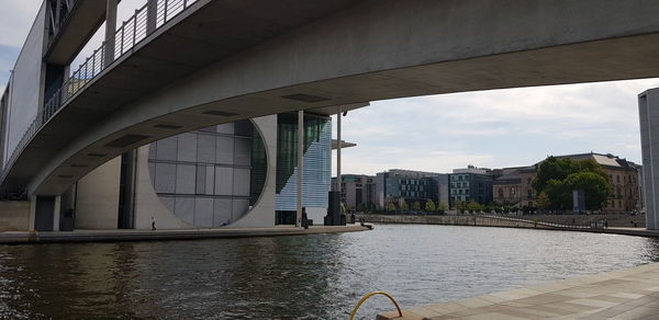 Bridge over river by buildings against sky