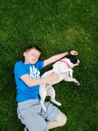 High angle view of boy sleeping with dog at grassy field