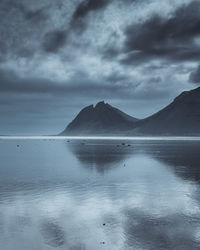 Scenic view of sea and mountains against storm clouds