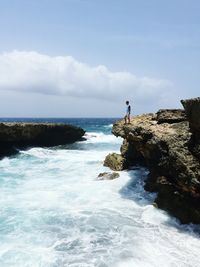 Man standing on rock formation by sea against cloudy sky