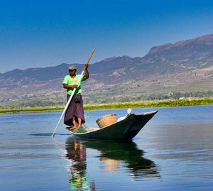 Man standing on boat in lake against sky