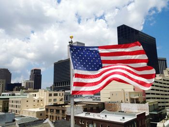 American flag by buildings against cloudy sky