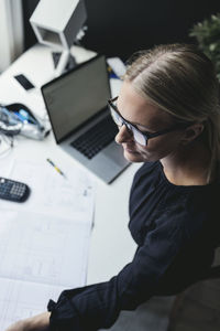 High angle view of female engineer with blueprint and laptop on desk