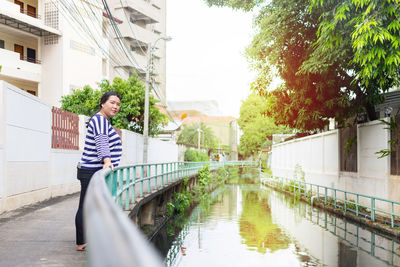 Young man in canal amidst buildings against trees