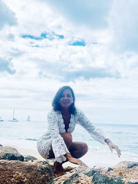 Portrait of woman sitting at beach by sea against sky