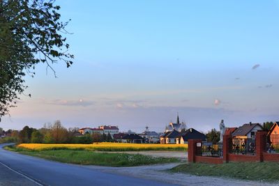 Road by buildings against sky during sunset in city