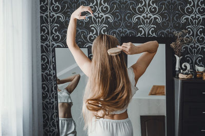Rear view of woman combing hair at home