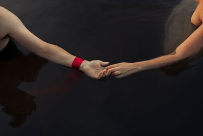 From above of crop anonymous traveler in wristband holding hand of girlfriend in pure lake