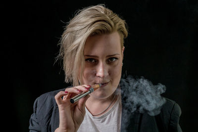 Portrait of young woman smoking against black background