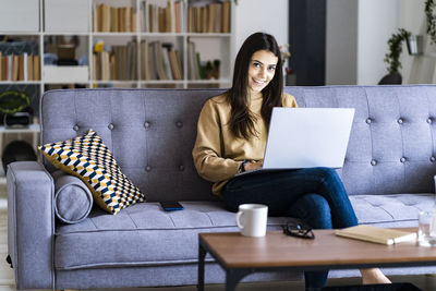 Woman using mobile phone while sitting on sofa at home