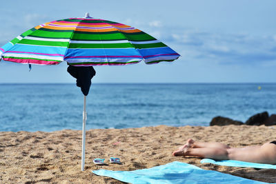 Low section of women relaxing by umbrella on beach