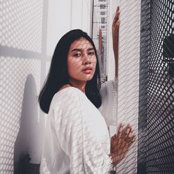 Portrait of beautiful young woman standing against window