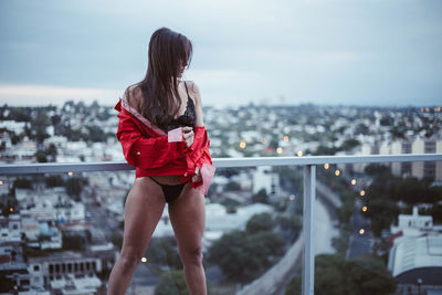 Woman standing in lingerie at balcony against cityscape