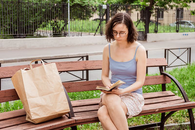 A girl reads a book on a bench in the city. interesting and useful leisure time alone
