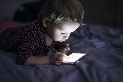 Toddler lying on bed playing with smartphone