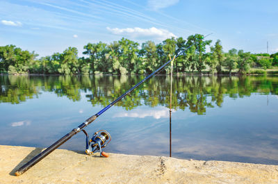 Fishing rod by lake against sky