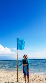 Woman standing by flag at beach against blue sky