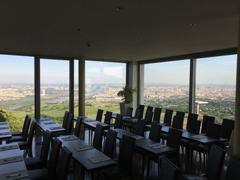 Empty chairs and tables against sky seen through window