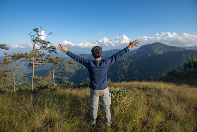 Rear view of man with arms outstretched standing on field against mountain