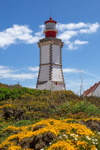 Low angle view of lighthouse on field by building against sky
