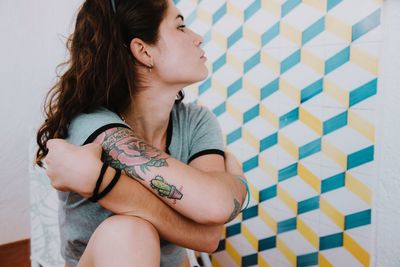 Young woman showing off her tattoo on arm while looking away at home