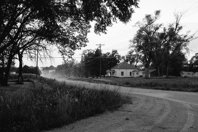 Road amidst trees and houses against sky